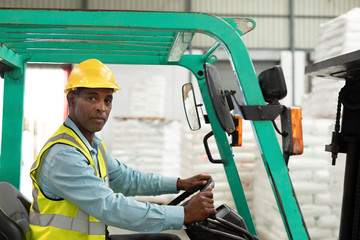Male worker sitting in forklift and looking at camera in warehouse