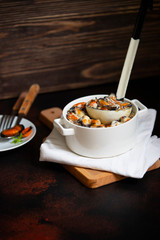 Mussels in cream and white wine sauce. Served with garlic and herbs in a white pan with a ladle. Seafood gourmet dish. Dark wooden background. Front view. Copyspace