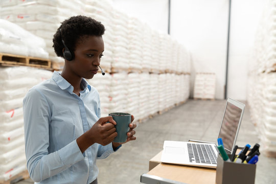 Female manager having coffee while working at desk in warehouse