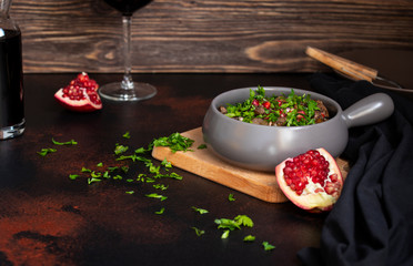 A traditional dish of Georgian cuisine Kuchmachi of chicken livers, hearts and gizzards with walnuts and pomegranate seeds. Served with herbs, pomegranate and red wine. Wooden background, front view