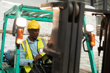 Male worker sitting in forklift and writing on clipboard in warehouse