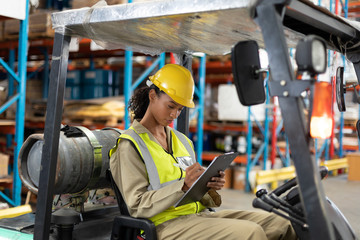 Female staff writing on clipboard while sitting on forklift
