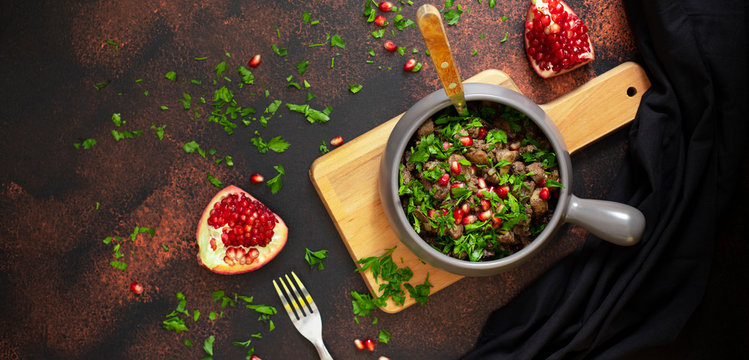 A traditional dish of Georgian cuisine Kuchmachi of chicken livers, hearts and gizzards with walnuts and pomegranate seeds. Served with fresh herbs and pomegranate in a clay plate. Top view, banner