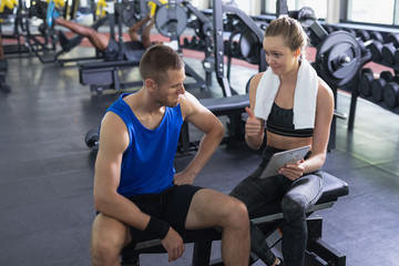 Female trainer and man interacting with each other while using digital tablet in fitness center