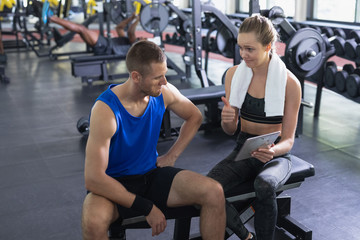 Fototapeta premium Female trainer and man interacting with each other while using digital tablet in fitness center