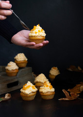 Pumpkin cupcakes on a dark backgroun. Female hand holding cupcake. Autumn background pumpkins and leaves. Pumpkin sweets. Halloween and Thanksgiving sweets. Selective focus. Copyspace. Vertical