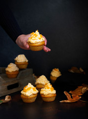 Pumpkin cupcakes on a dark backgroun. Female hand holding cupcake. Autumn background pumpkins and leaves. Pumpkin sweets. Halloween and Thanksgiving sweets. Selective focus. Copyspace. Vertical