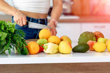 pretty young woman cutting orange by knife on wooden board in kitchen