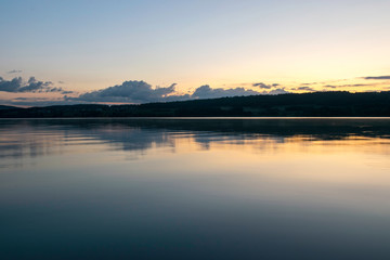 Obraz premium view of the lake at dawn early in the morning, silhouettes of hills and clouds