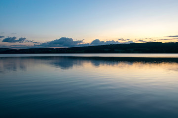 view of the lake at dawn early in the morning, silhouettes of hills and clouds
