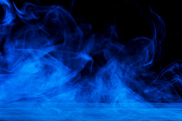 Conceptual image of blue smoke isolated on dark black background and wooden table.