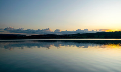 view of the lake at dawn early in the morning, silhouettes of hills and clouds