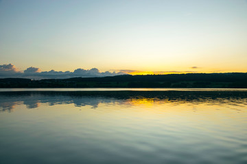 view of the lake at dawn early in the morning, silhouettes of hills and clouds