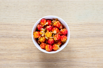 white ceramic round bowl with bright red-orange cloudberry on wooden table, top view