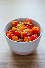 bright yellow-red cloudberries in a ceramic bowl on a wooden table, vertical frame