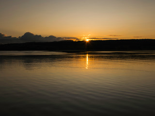 early morning on the lake, dusk, sun rising behind the hill
