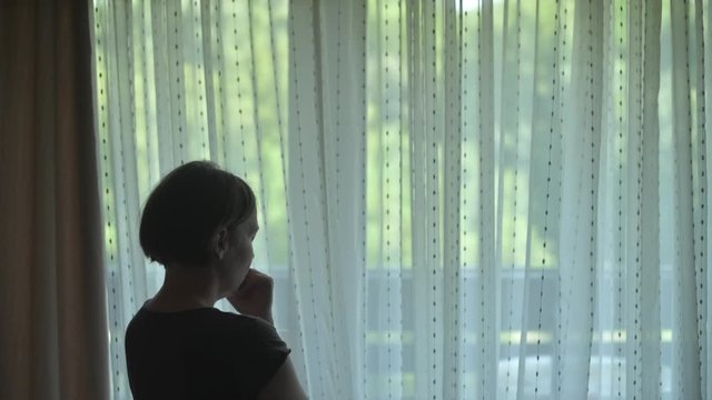 Rear view of sad alone woman looking out the window and thinking. Casual sorrowful female person is feeling lonely, handheld footage