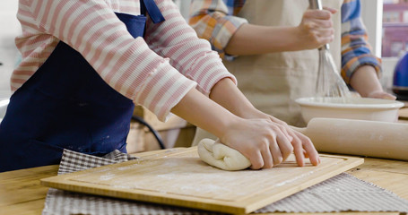Obraz premium Little girl kneading flour with her mother whisking dough in bowl in background. close up photo focus on hand unrecognized face parent and child having fun diy baking cake at home in kitchen easter