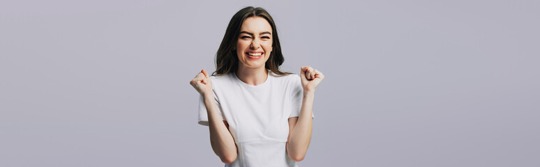 excited beautiful girl in white t-shirt showing yes gesture isolated on grey, panoramic shot