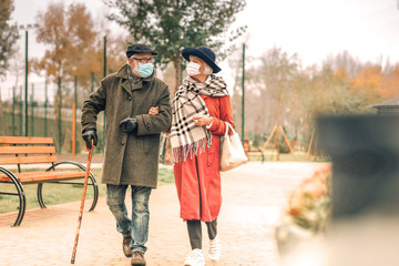 Stylish senior couple wearing face masks walking in park together