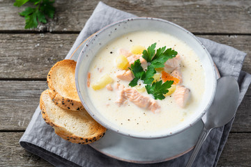 Finnish salmon soup with cream and parsley in grey bowl on an old wooden background. Rustic style....