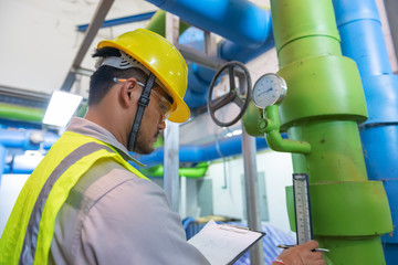 Asian engineer wearing glasses working in the boiler room,maintenance checking technical data of heating system equipment,Thailand people