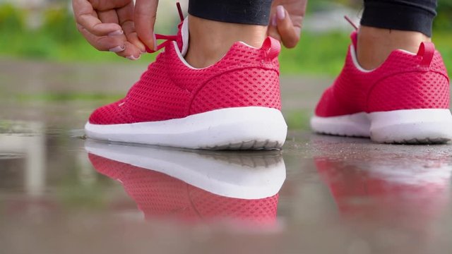 Running in rainy weather. Woman ties her shoelaces and starts to run. Back view. Slow motion