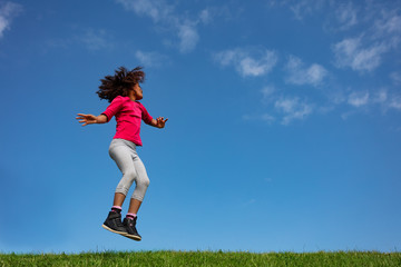 Happy curly hair girl jump over blue sky side view