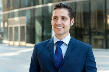 Portrait of happy young businessman in blue suit in front of glass skyscrapers