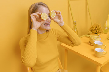 Woman holding lemons in front of eyes in a yellow scene