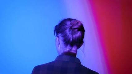 Back view of young woman looking around at modern immersive exhibition or club event with changing multi color projector light illumination. Digital art, technology and entertainment concept