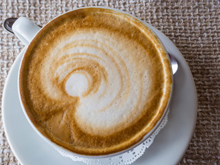 coffee cappuccino or latte in white elegant cup with saucer, on rustic sackcloth a background. Morning hot beverage. Coffee lifestyle.