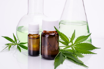 Medical, chemical theme background with cannabis leaves, oil bottle and laboratory glass flasks behind on a white.