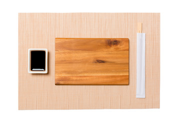 Empty rectangular brown wooden plate with chopsticks for sushi and soy sauce on brown sushi mat background. Top view with copy space for you design