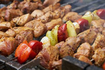 pieces of meat are friend on fire on skewers on grill with veg. close up