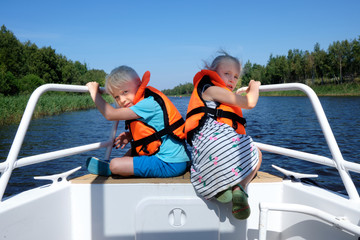 Children sail on a boat on the river. A little boy and girl in life vests travel by boat. Children...