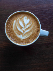 Hot coffee in a cup with foam milk beautiful latte art on wooden table background. Cappuccino or latte with froth foam