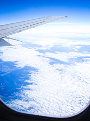 View from the airplane porthole on white clouds. The frame also shows the wing of the aircraft. Travel Photo.