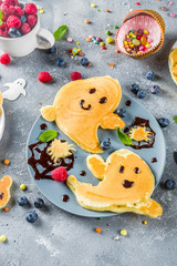 Halloween kids food treat. Funny pancakes - ghosts, jack o Lantern pumpkins, spider webs. Breakfast snack for child's Halloween party, with berries & candy,  gray stone table top view copy space