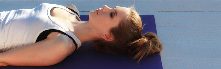 Young woman practicing yoga outdoors. Girl in shavasana on purple mat on white wooden floor. Portrait in profile close up.