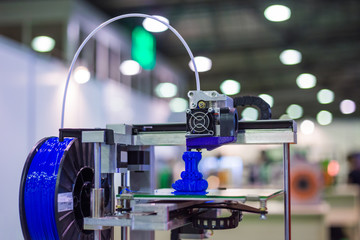 Automatic three dimensional 3D printer machine printing plastic model of blue toy dragon at modern technology exhibition. 3D printing, additive technologies and futuristic concept