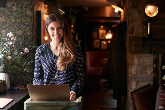 Portrait Of Female Receptionist Working On Laptop At Hotel Check In