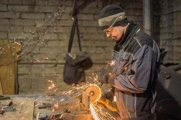 Professional blacksmith sawing metal with hand circular saw at forge, workshop. Handmade, craftsmanship and blacksmithing concept