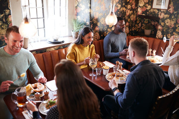 Group Of People Eating In Restaurant Of Busy Traditional English Pub - Powered by Adobe