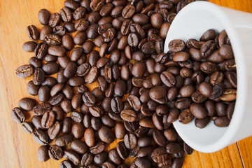 full of coffee beans spilling out white ceramic cup on brown wooden background