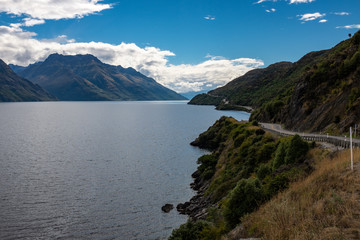 A highway weaves it's way along side Lake Te Anau in New Zealand and disappears into the distance surronded by mountains and dense forests
