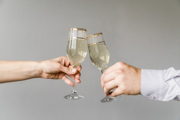 Friends hands clinking glasses of champagne on grey background