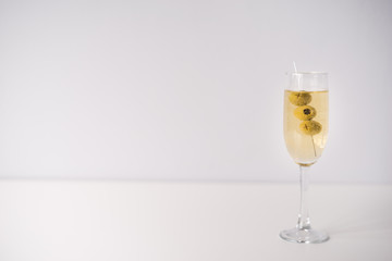 Glass of alcoholic drink with olives on white background
