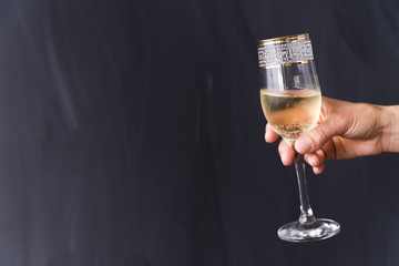 A person's hand holding elegant champagne glass with bubble against black background