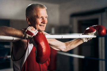 Happy funny senior boxer man with red gloves in the ring